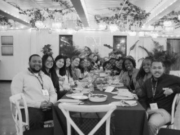 Group of UM students and alum sitting at a long table, leaning in to be seen by the camera